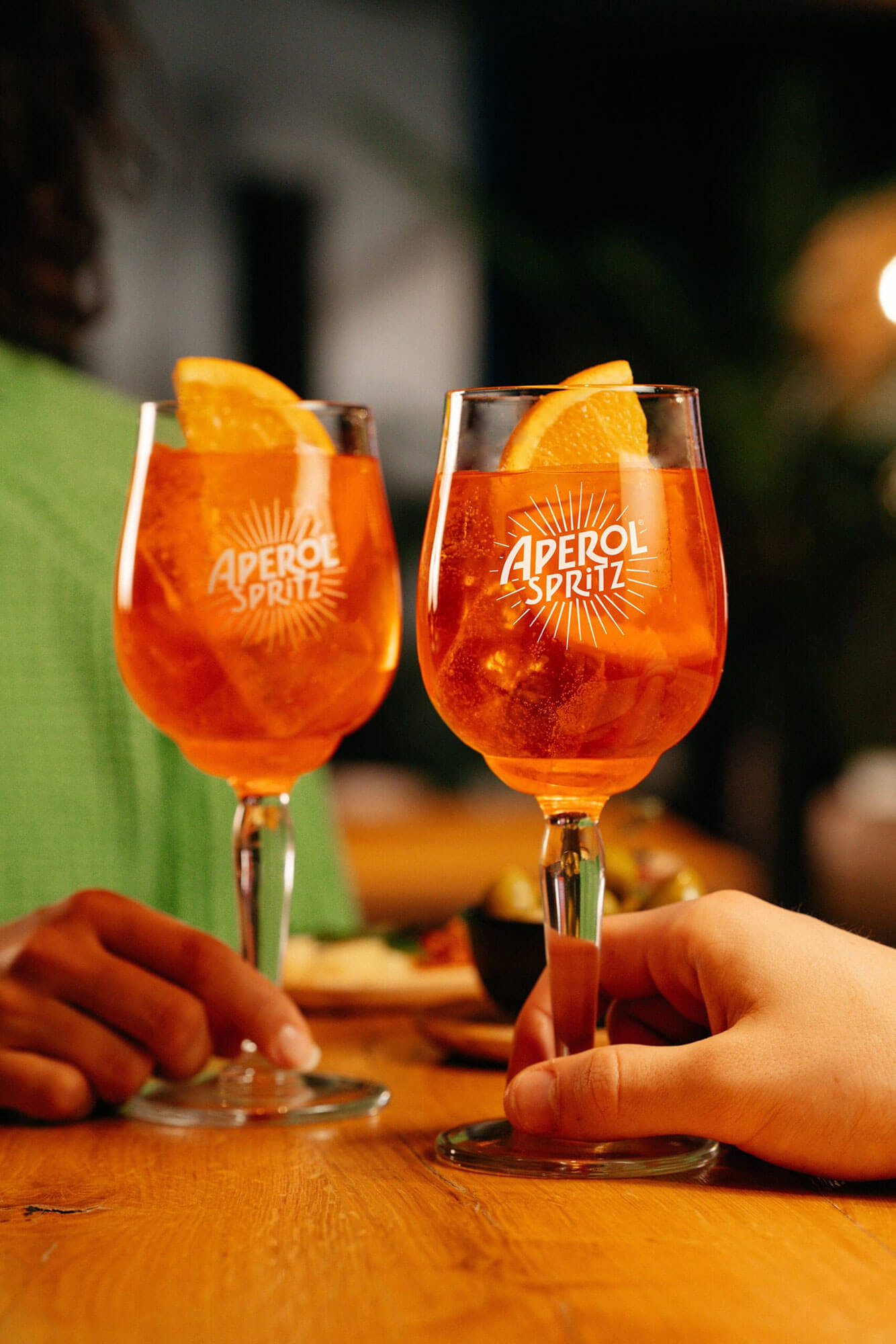 Zwei Gläser Aperol Spritz mit Orangenscheiben beim gemeinsamen Anstoßen